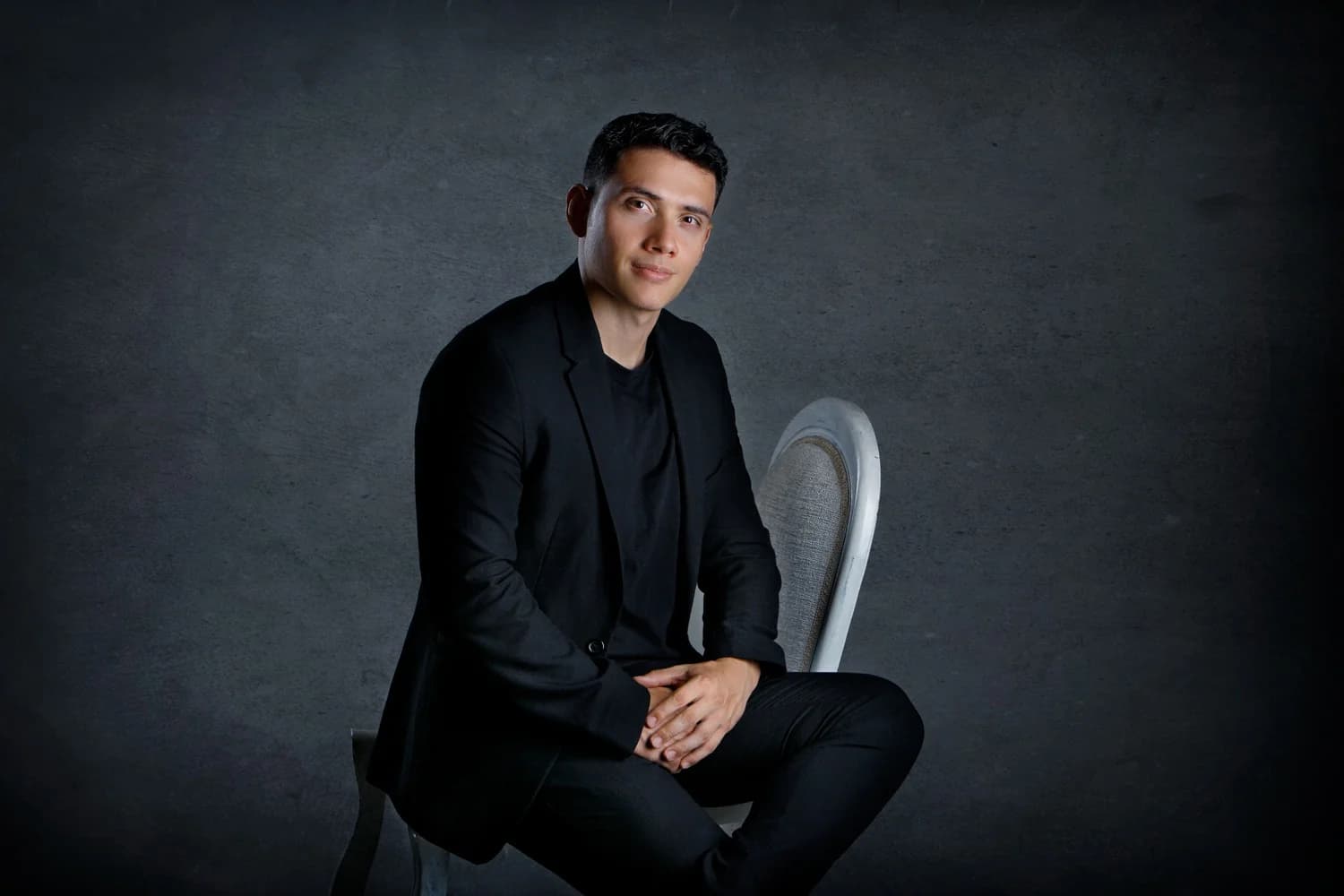 Carlos Medina sentado, retrato editorial sobre fondo oscuro
